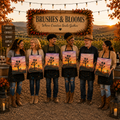 Six people standing outdoors at sunset holding square paintings of a desert sunset with a silhouetted tree, under a wooden sign that reads 'Brushes & Blooms Where Creative Souls Gather.'.